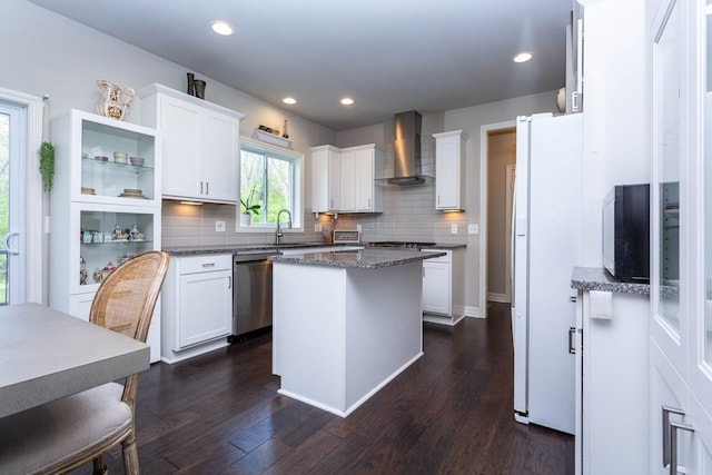 kitchen with a sink, stainless steel appliances, white cabinets, backsplash, and wall chimney range hood
