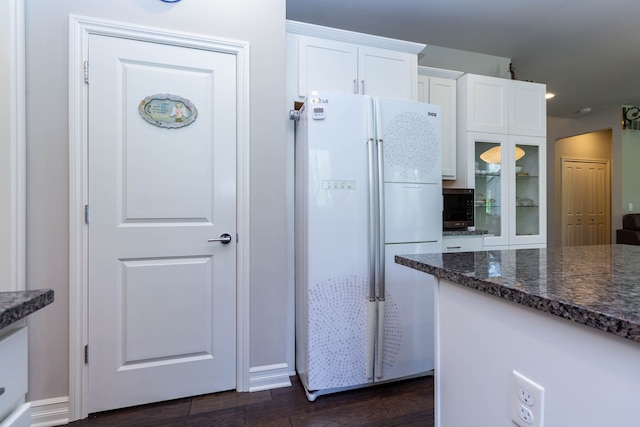 kitchen featuring freestanding refrigerator, dark wood-style flooring, dark stone countertops, and white cabinetry