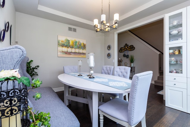 dining area with a tray ceiling, dark wood finished floors, visible vents, stairway, and a chandelier