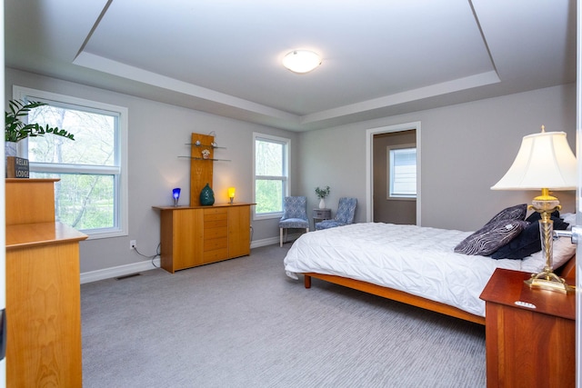 carpeted bedroom featuring a tray ceiling and baseboards