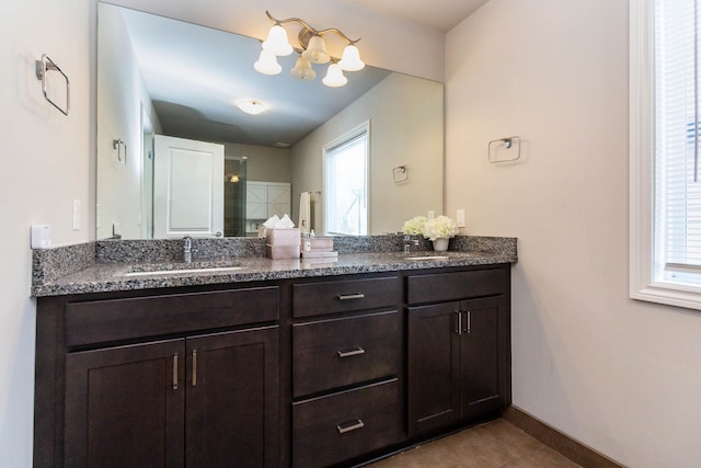 full bathroom with baseboards, a chandelier, double vanity, and a sink