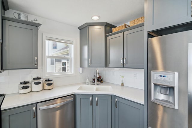 kitchen featuring stainless steel appliances, gray cabinetry, a sink, light countertops, and tasteful backsplash
