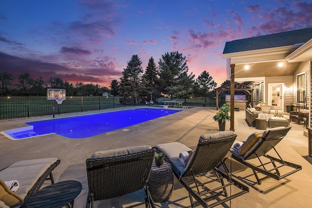 pool at dusk with fence, outdoor lounge area, and a patio area