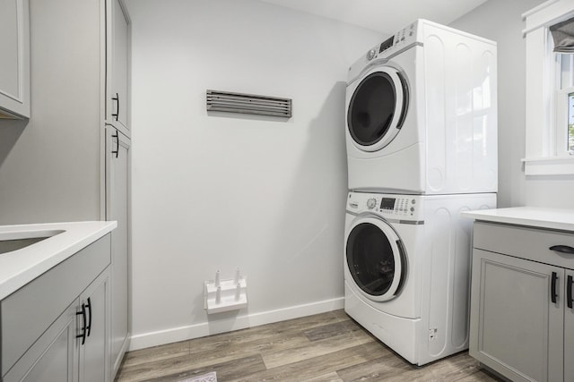 washroom with baseboards, stacked washing maching and dryer, light wood-style flooring, and cabinet space