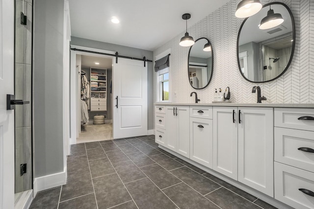 bathroom featuring an enclosed shower, double vanity, a walk in closet, tile patterned floors, and visible vents