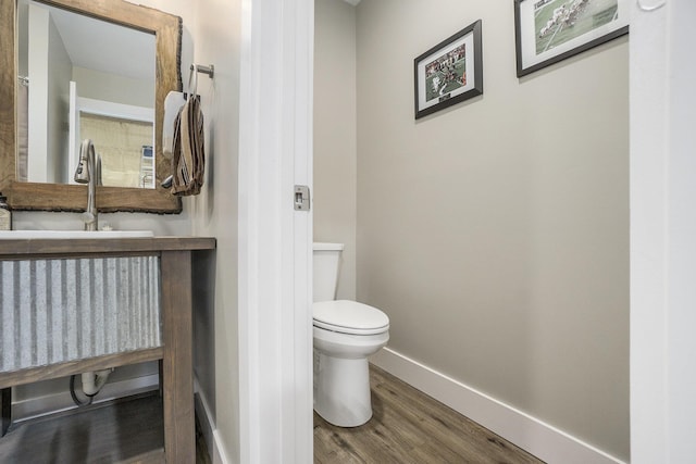 half bathroom with a sink, toilet, baseboards, and wood finished floors