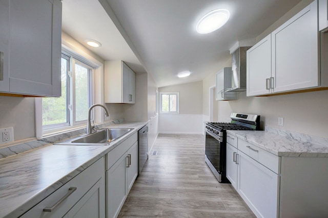 kitchen featuring stainless steel appliances, a sink, light wood finished floors, light countertops, and wall chimney range hood