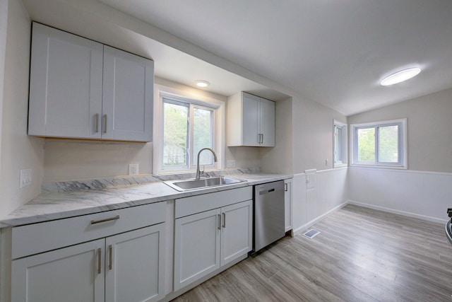 kitchen with stainless steel dishwasher, a sink, vaulted ceiling, light wood-style floors, and white cabinets