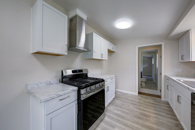 kitchen with stainless steel range with gas cooktop, wall chimney range hood, white cabinetry, baseboards, and light wood finished floors