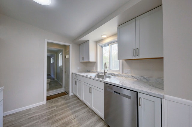 kitchen with dishwasher, a sink, vaulted ceiling, white cabinets, and light wood-style flooring
