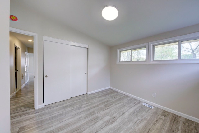 unfurnished bedroom featuring light wood-type flooring, vaulted ceiling, baseboards, and a closet