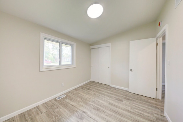 unfurnished bedroom featuring vaulted ceiling, light wood-style floors, baseboards, and a closet
