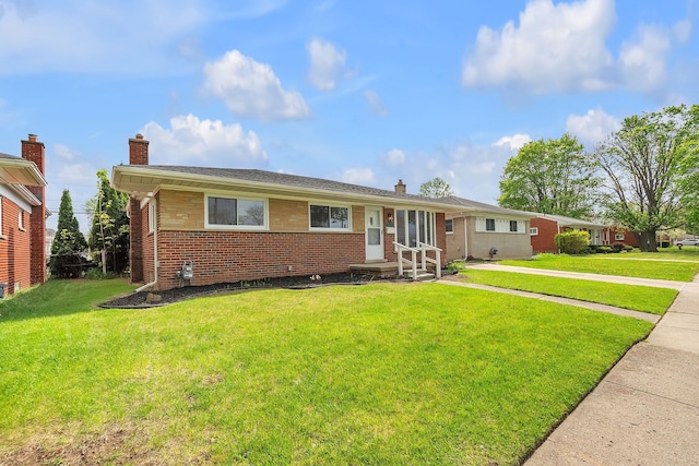 ranch-style house featuring entry steps, a front yard, a chimney, and brick siding