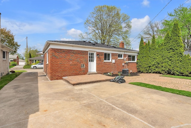 rear view of house with brick siding, a patio, and a chimney