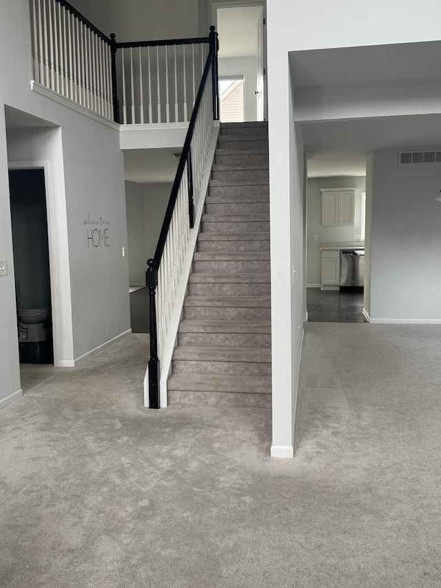 staircase featuring carpet, visible vents, baseboards, and a high ceiling