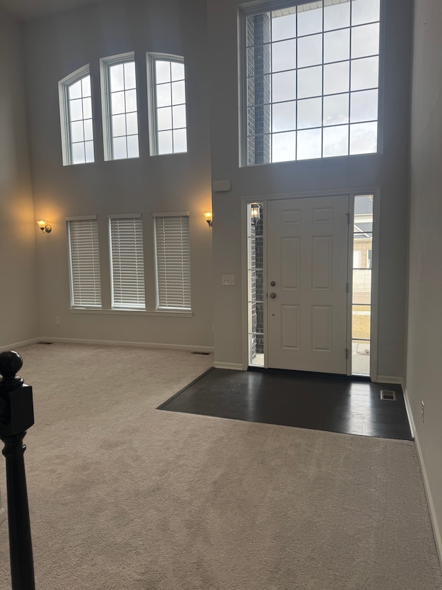 carpeted foyer featuring a towering ceiling and baseboards