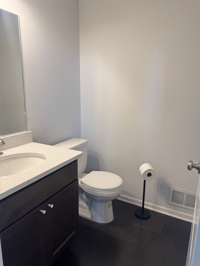half bath with toilet, visible vents, wood finished floors, and vanity