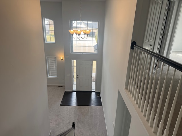 carpeted foyer featuring baseboards, a notable chandelier, and a high ceiling
