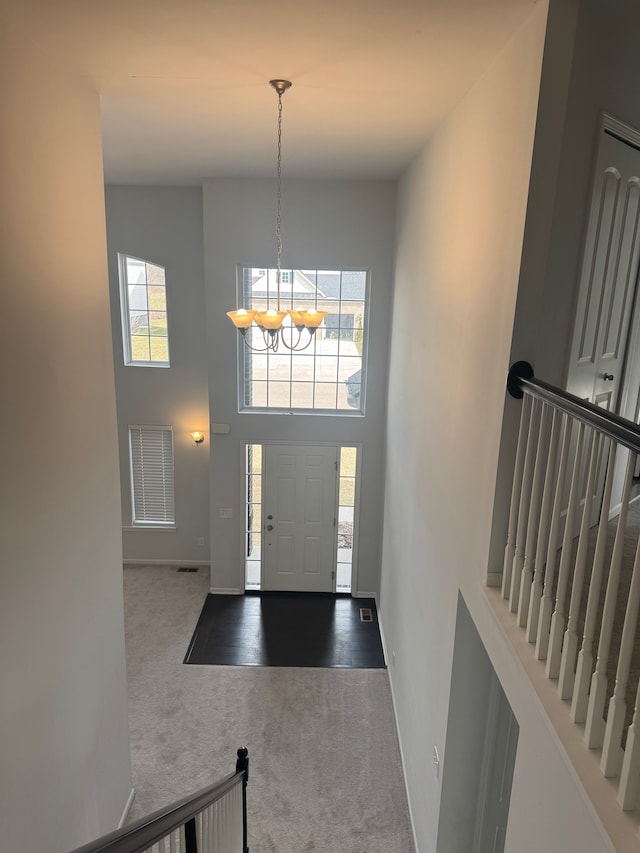 foyer entrance with carpet flooring, an inviting chandelier, baseboards, and a towering ceiling