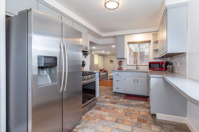 kitchen with appliances with stainless steel finishes, tasteful backsplash, light countertops, under cabinet range hood, and a sink