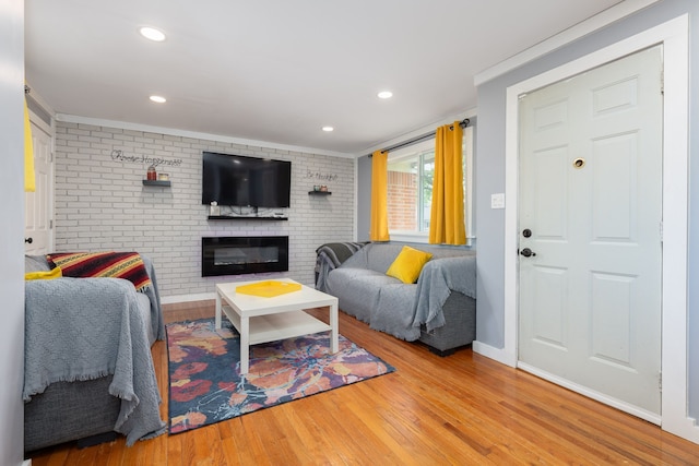 living room featuring brick wall, wood finished floors, a brick fireplace, ornamental molding, and baseboards