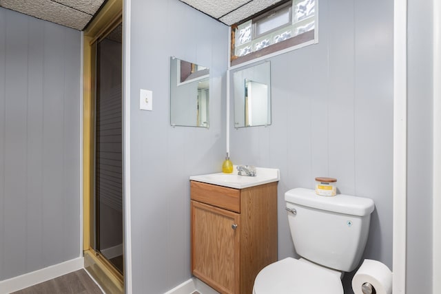 bathroom featuring toilet, vanity, wood finished floors, a shower with shower door, and baseboards