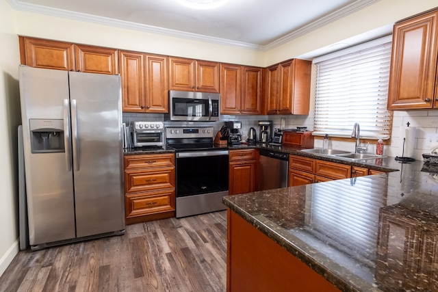 kitchen featuring a sink, brown cabinetry, crown molding, appliances with stainless steel finishes, and dark wood-style floors
