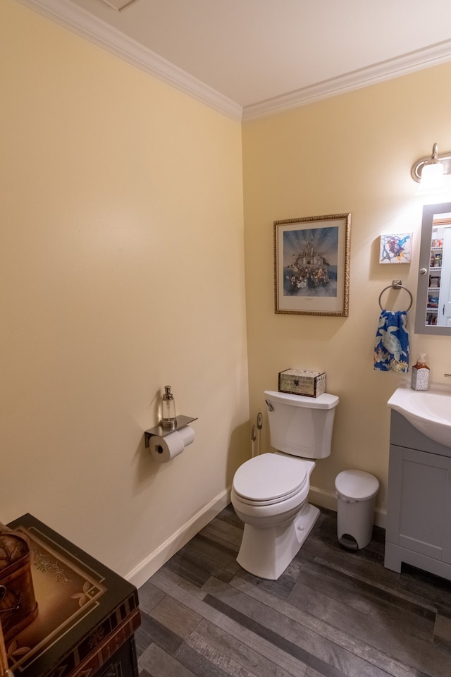 half bath with toilet, baseboards, vanity, crown molding, and wood finished floors