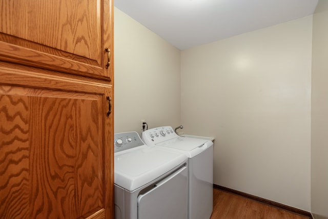 laundry area with baseboards, washer and dryer, light wood-type flooring, and cabinet space