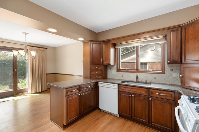 kitchen with white appliances, a healthy amount of sunlight, a sink, a peninsula, and a chandelier