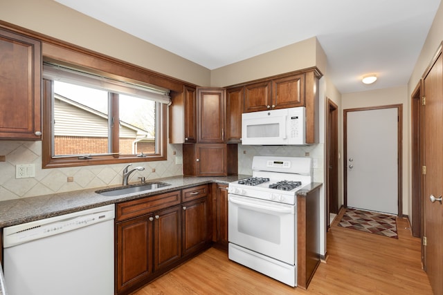 kitchen with backsplash, white appliances, light wood-style flooring, and a sink