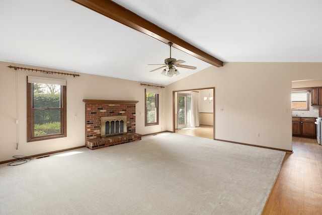 unfurnished living room with a brick fireplace, lofted ceiling with beams, a ceiling fan, and plenty of natural light