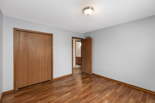 unfurnished bedroom featuring a closet, baseboards, visible vents, and wood finished floors