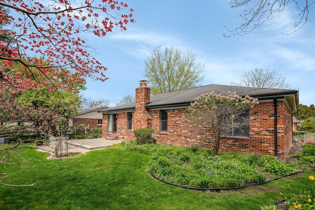 rear view of house featuring a chimney, a yard, a patio, and brick siding
