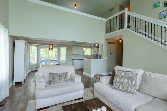living area with dark wood-type flooring, a towering ceiling, baseboards, and stairs