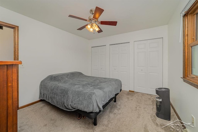 carpeted bedroom featuring two closets, baseboards, and ceiling fan
