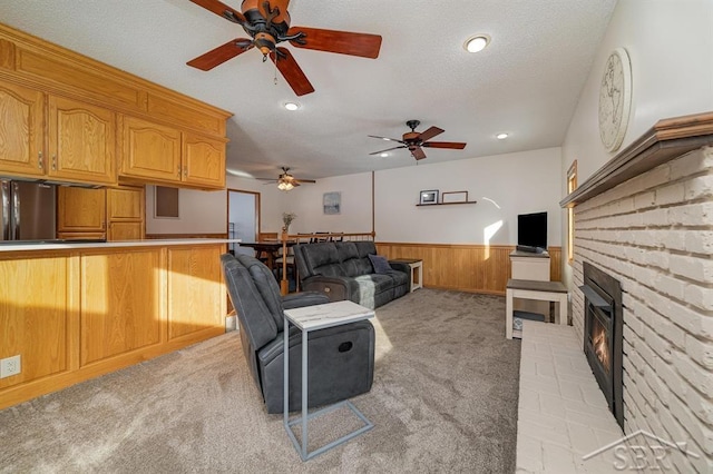 living room featuring a ceiling fan, a fireplace, wainscoting, light colored carpet, and recessed lighting