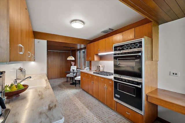 kitchen featuring brown cabinetry, dobule oven black, visible vents, light countertops, and stainless steel gas cooktop