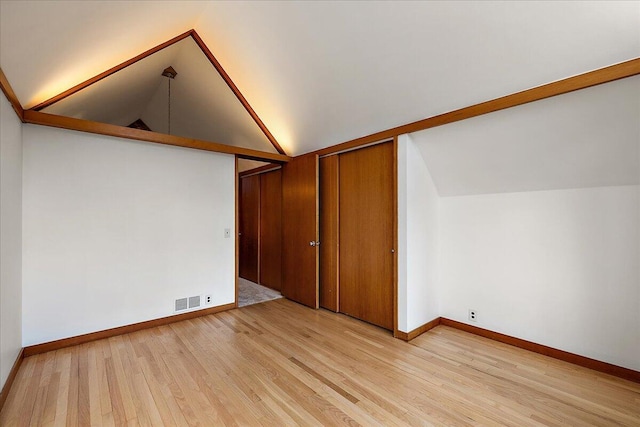 additional living space with light wood-style floors, vaulted ceiling, baseboards, and visible vents