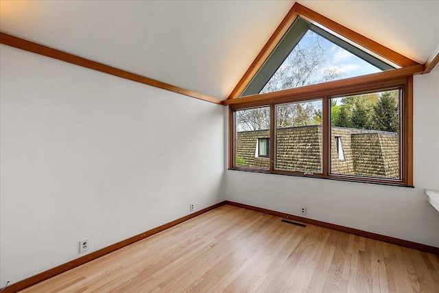 empty room with baseboards, light wood finished floors, visible vents, and vaulted ceiling