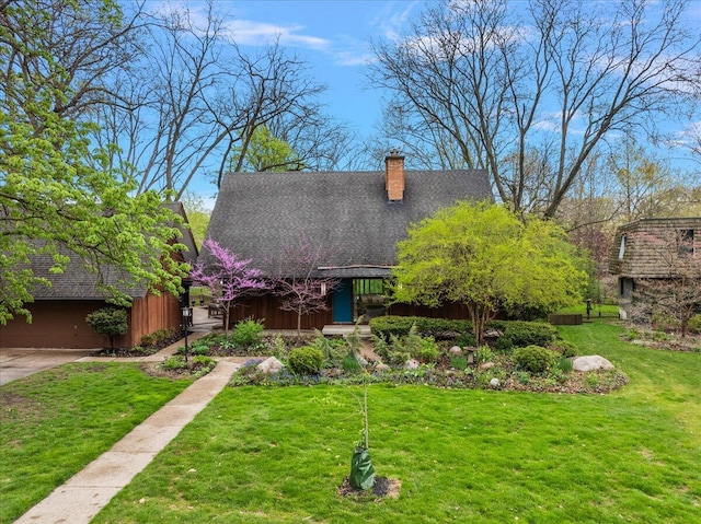 view of front facade featuring a chimney, a front yard, and a shingled roof