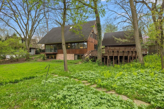 back of house featuring a sunroom, a deck, a shingled roof, a yard, and stairs