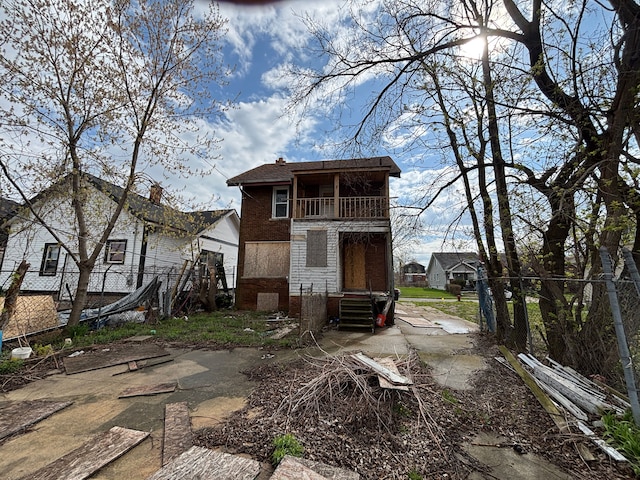 back of property featuring a balcony, brick siding, and fence