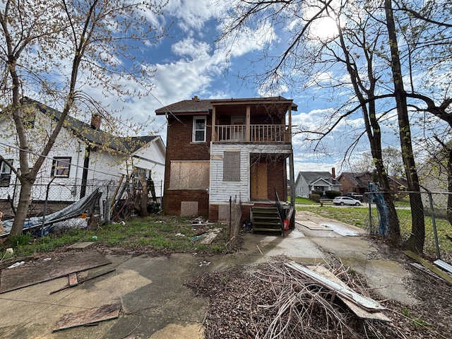 rear view of property featuring a balcony, brick siding, and fence