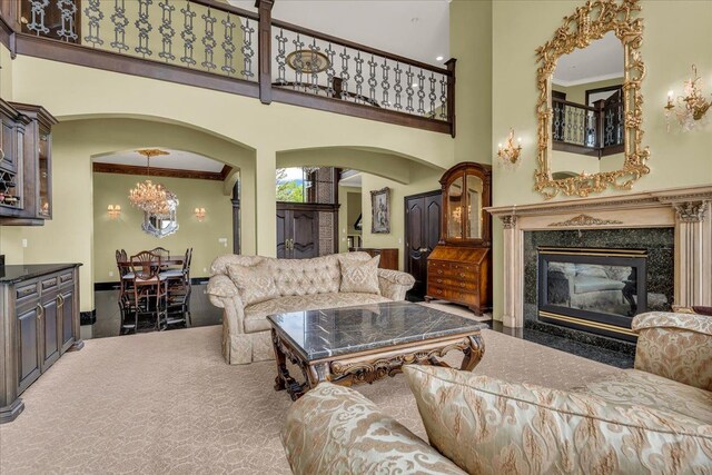 carpeted living area featuring arched walkways, a premium fireplace, an inviting chandelier, and a towering ceiling
