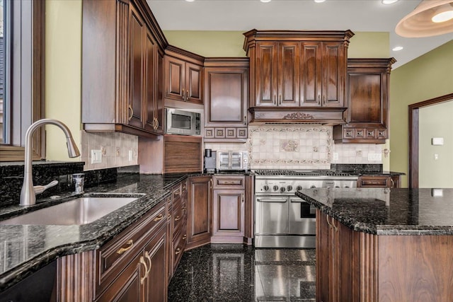 kitchen with granite finish floor, a sink, premium range hood, dark stone counters, and appliances with stainless steel finishes