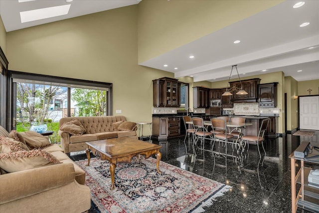 living area featuring granite finish floor, recessed lighting, baseboards, a towering ceiling, and a skylight