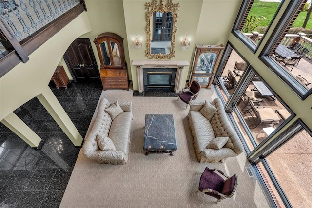 living room with a high end fireplace, granite finish floor, visible vents, and a towering ceiling