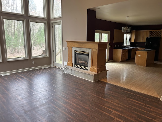 unfurnished living room featuring visible vents, a sink, a chandelier, wood finished floors, and a tile fireplace