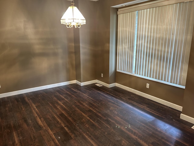 empty room featuring baseboards, an inviting chandelier, and dark wood-style floors